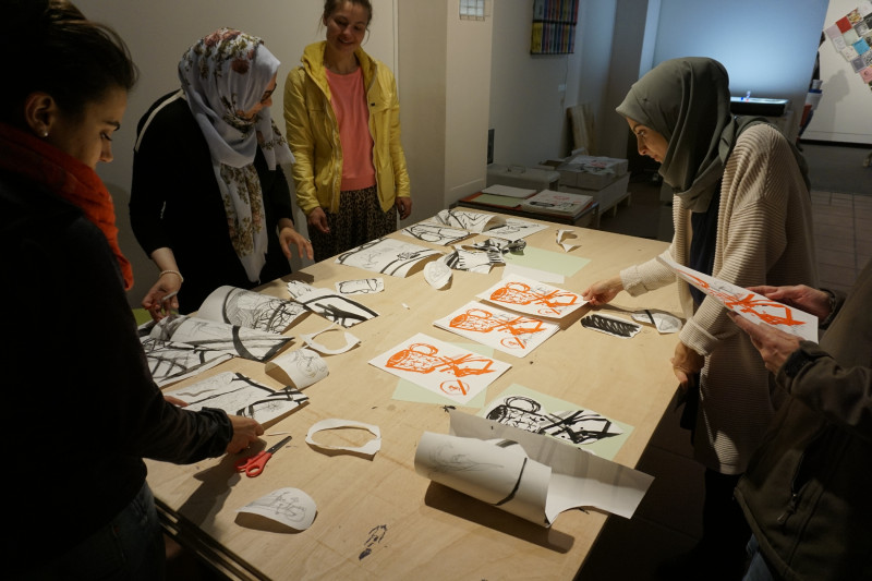 Frauen stehen um einen Tisch und schauen sich Drucke von Zeichnungen an