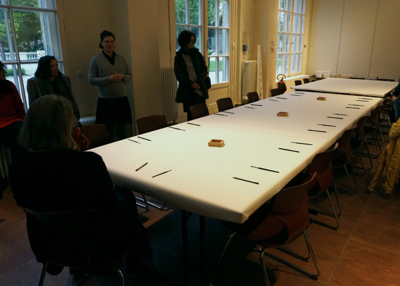 Großer langer Tisch ist mit weißen Papier bedeckt, darauf sind Pinsel und Stifte wie Besteck platziert