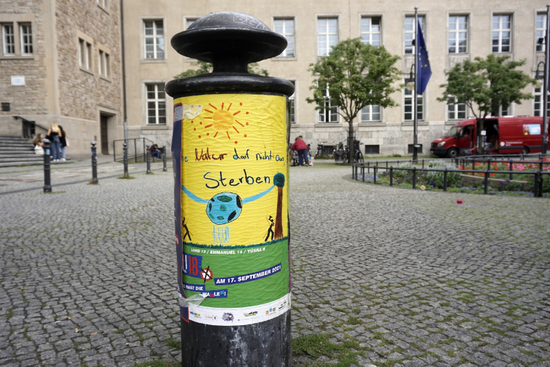 Plakat auf Hydraten geklebt, Gebäude ist im Hintergrund zu sehen