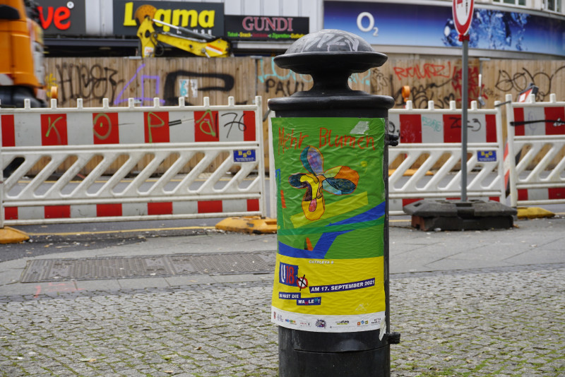 Buntes Plakat auf Hydrantem, Baustelle ist im Hintergrund zu sehen