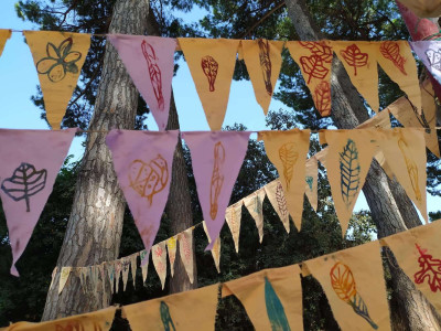 Bunte Wimpel mit Pflanzendrucken darauf sind auf langen Schnüren zwischen Bäumen aufgehangen